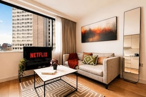 A modern living room with a sofa, a coffee table, a TV displaying 'NETFLIX', and a city view through the window. - Modern Studio by Stay With Us (Salford)