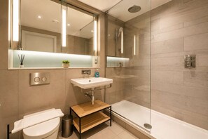 A modern bathroom with a glass shower enclosure, a white sink, and a toilet. - Modern Studio by Stay With Us (Salford)