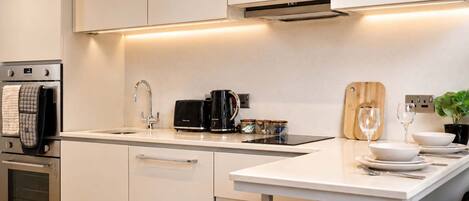 A modern kitchen with stainless steel appliances, a white countertop, and a wooden cutting board.