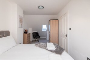 Ein Schlafzimmer mit einem Bett, einem Schreibtisch, einem Stuhl, einem Kleiderschrank und einer Tür.