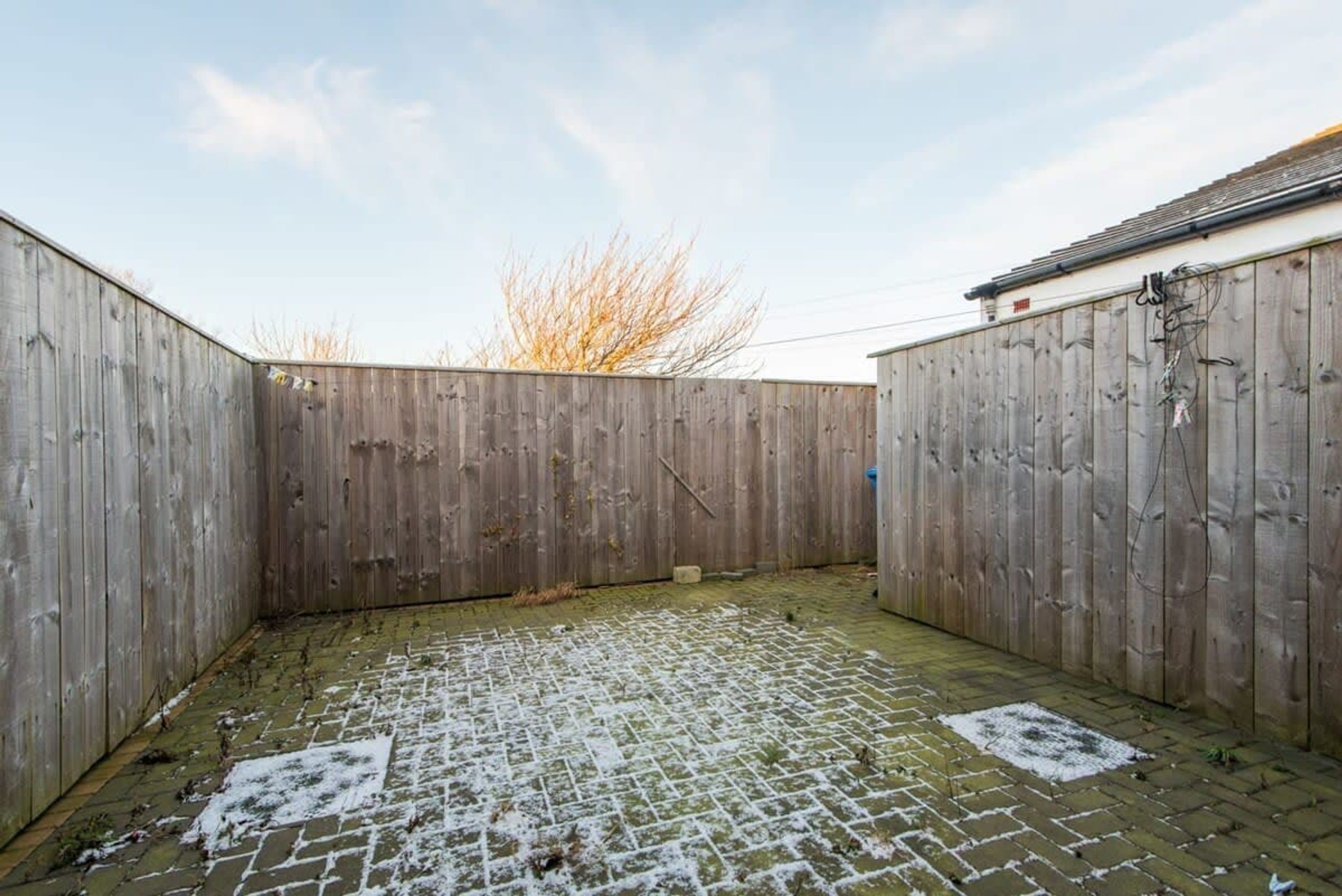 A courtyard with a wooden fence, a brick floor, and a building with a tiled roof.