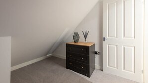 Une pièce avec un plafond en pente, une porte blanche et un meuble de rangement noir doté de tiroirs.