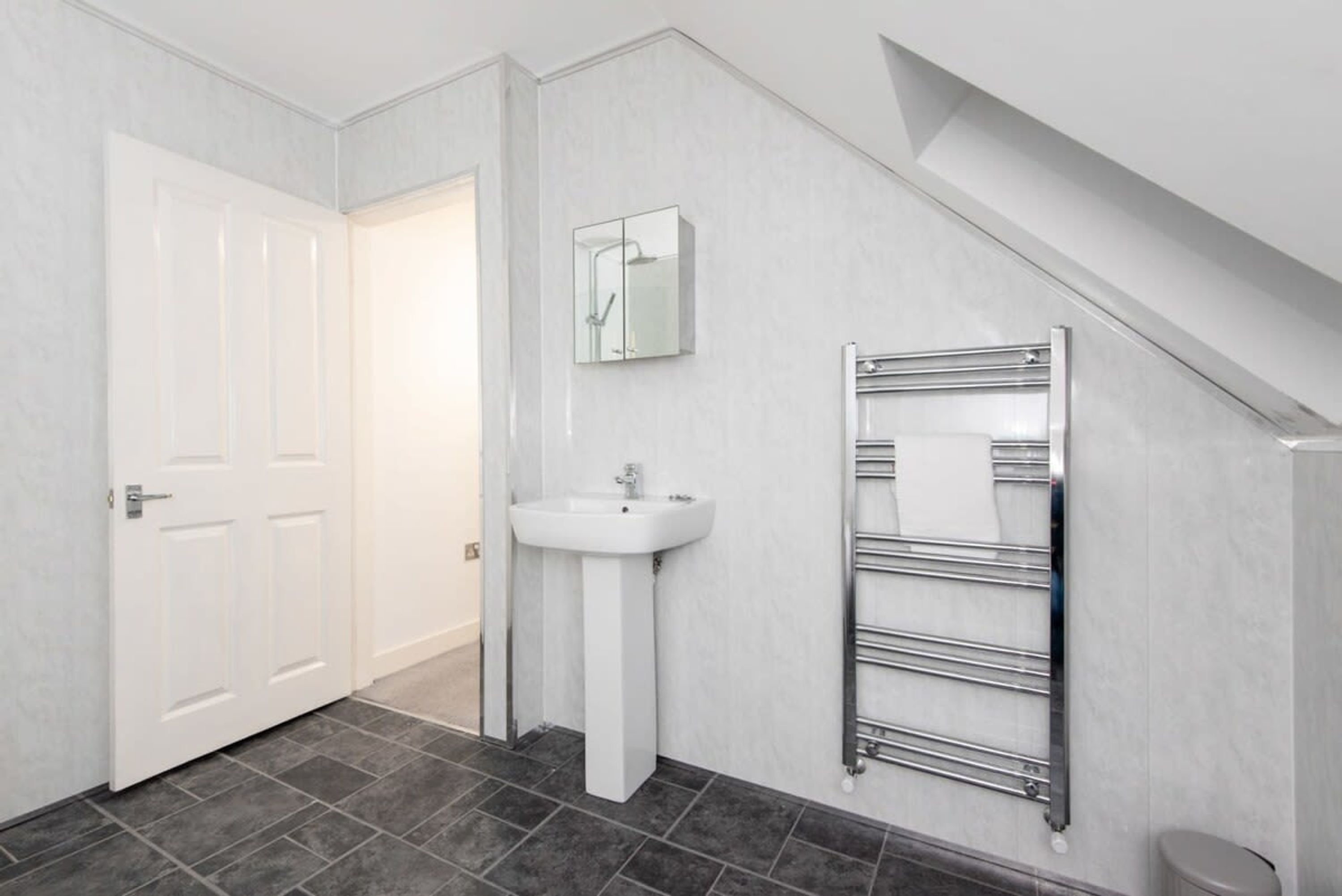 A bathroom with a white door, a sink, a mirror, and a towel rack.
