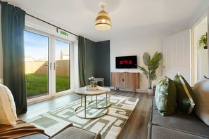 Uma sala de estar moderna com uma ampla porta de vidro deslizante, uma televisão de tela plana, uma mesa de centro redonda e um sofá.