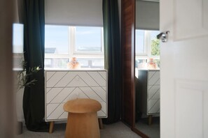 Una habitación con un mueble de estilo geométrico en blanco y negro, un taburete de madera y vistas al exterior a través de una ventana.