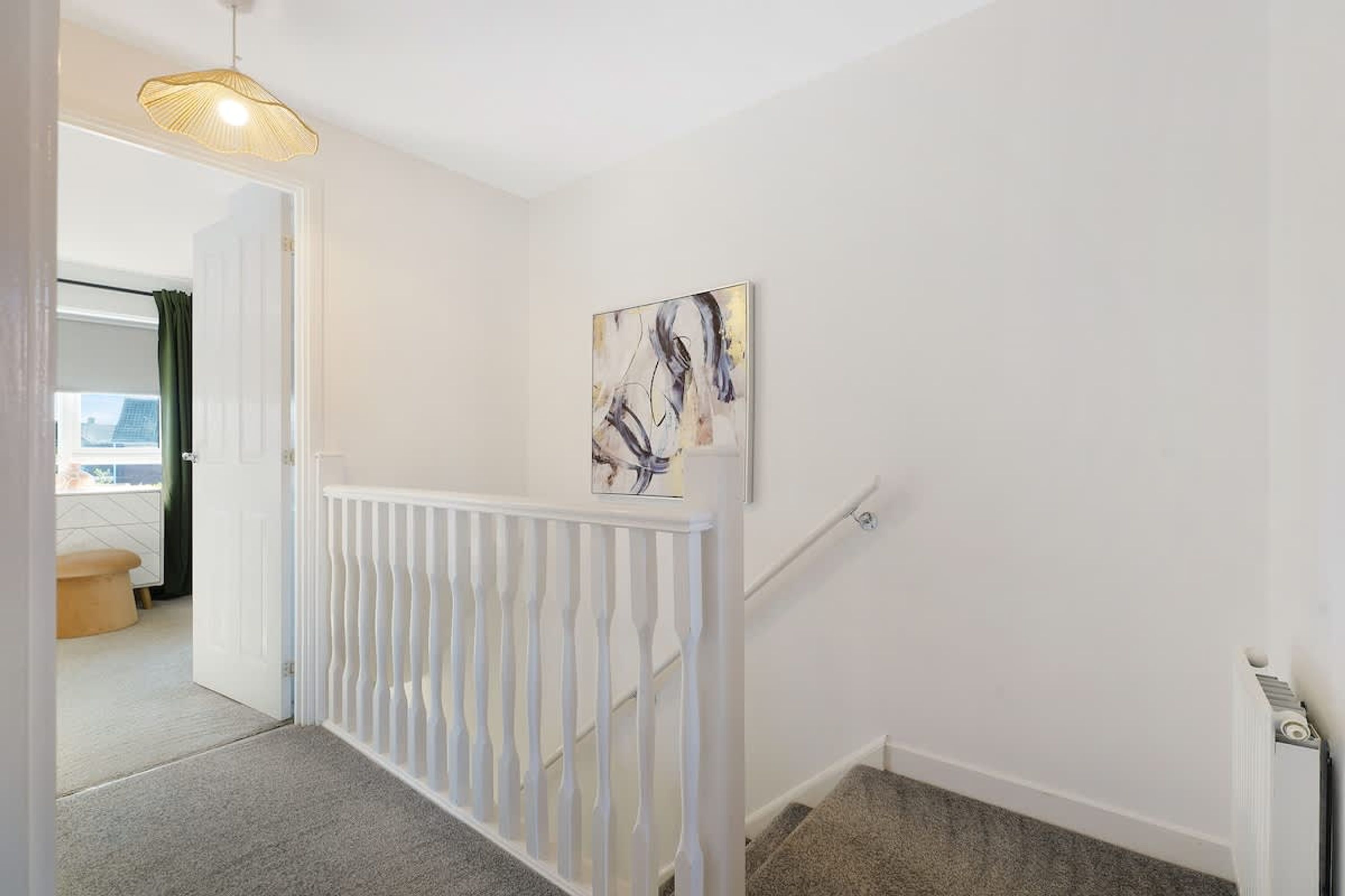 A hallway with a white railing, a painting on the wall, and a door leading to another room.