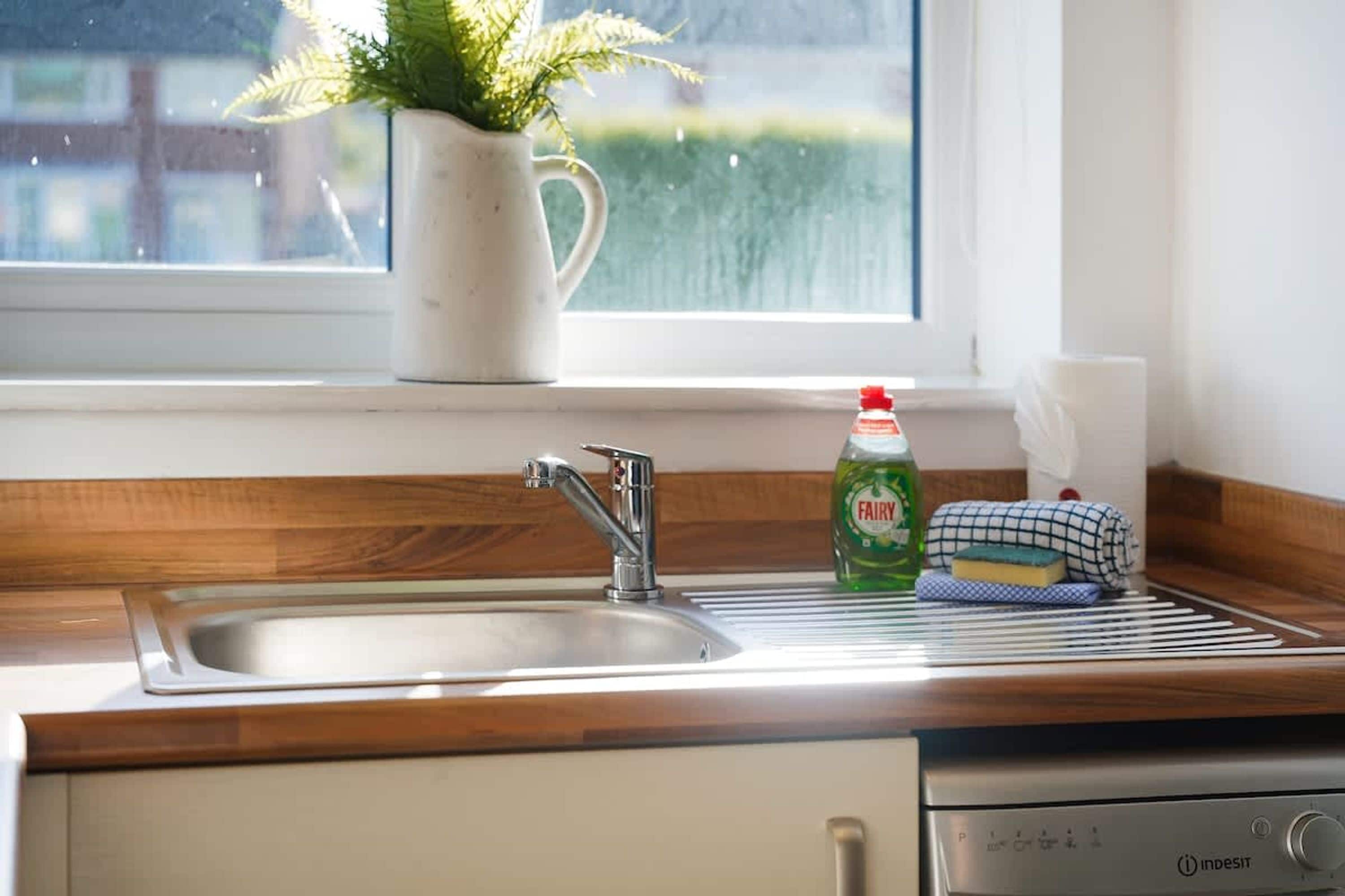 A kitchen with a stainless steel sink, a dish soap bottle, a sponge, and a dish towel on the counter.