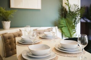 A dining table set with white plates, bowls, and wine glasses, with a cushioned bench and a potted plant in the background. - Modern Coastal Stay Minutes From Redcar Beach (Redcar)