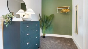 A room with a dark blue dresser, a round mirror, two white lamps, a green wall, a plant, a coat rack, and a framed picture. - Hartlepool Marina Retreat 2BR Sleeps 4 by Stay With Us (Hartlepool)
