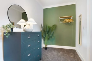 A room with a dark blue dresser, a round mirror, two white lamps, a green wall, a plant, a coat rack, and a framed picture. - Hartlepool Marina Retreat 2BR Sleeps 4 by Stay With Us (Hartlepool)