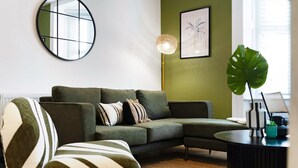 A modern living room with a sectional sofa, a round mirror, a floor lamp, and a large plant. - Hartlepool Marina Retreat 2BR Sleeps 4 by Stay With Us (Hartlepool)