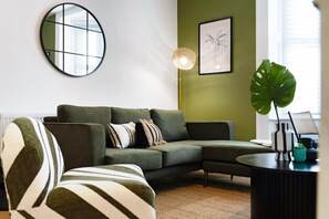 A modern living room with a sectional sofa, a round mirror, a floor lamp, and a large plant. - Hartlepool Marina Retreat 2BR Sleeps 4 by Stay With Us (Hartlepool)