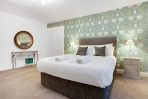 A neatly made bed with white linens and two pillows, a small bedside table with a lamp, a round mirror on the wall, and a green stool. - Luxurious Hot Tub Getaway Cottage Free Parking (Bishop Auckland)