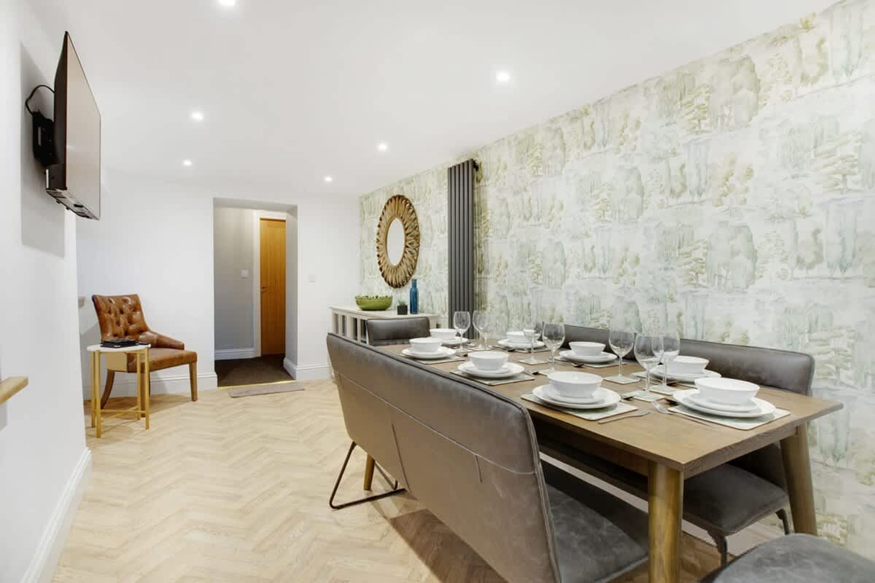 Un comedor con una mesa larga dispuesta para seis personas, un televisor montado en la pared y una puerta que da a otra habitación.