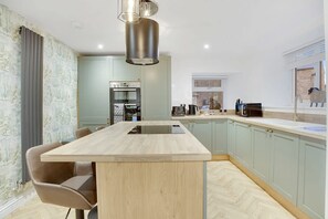 A modern kitchen with a central island, built-in appliances, and a view of a cityscape. - Luxurious Hot Tub Getaway Cottage Free Parking (Bishop Auckland)
