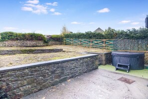 A stone wall, a wooden fence, and a large black container in an outdoor area. - Luxurious Hot Tub Getaway Cottage Free Parking (Bishop Auckland)