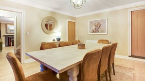 Ein Esszimmer mit einem großen Holztisch, sechs gepolsterten Stühlen, einem runden Spiegel, einem gerahmten Kunstwerk und einer Tür.