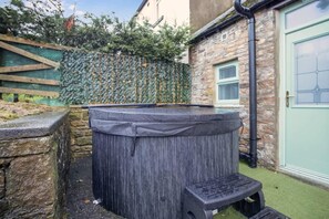 Un jacuzzi en un jardín con muro de piedra y cerca de madera.