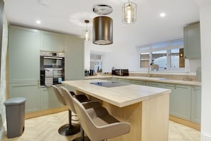 A modern kitchen with a central island, bar stools, built-in appliances, and pendant lighting. - Luxurious Hot Tub Getaway Cottage Free Parking (Bishop Auckland)