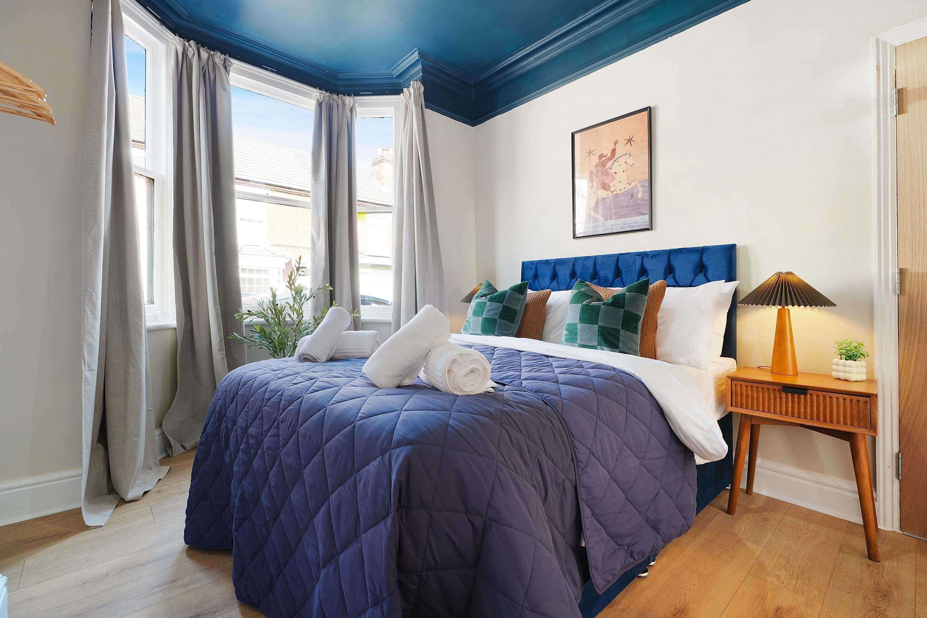 Une chambre à coucher avec un grand lit, une table de chevet avec une lampe et une fenêtre avec des rideaux.