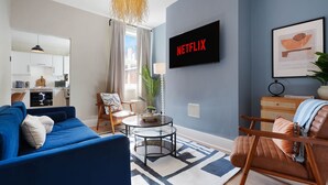 Ein modernes Wohnzimmer mit einem blauen Sofa, einem Couchtisch und einem Fernseher, der 'NETFLIX' anzeigt.