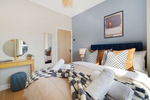 Ein Schlafzimmer mit einem Bett, Nachttischen, einem Spiegel, einer Tür und einem gerahmten Bild an der Wand.