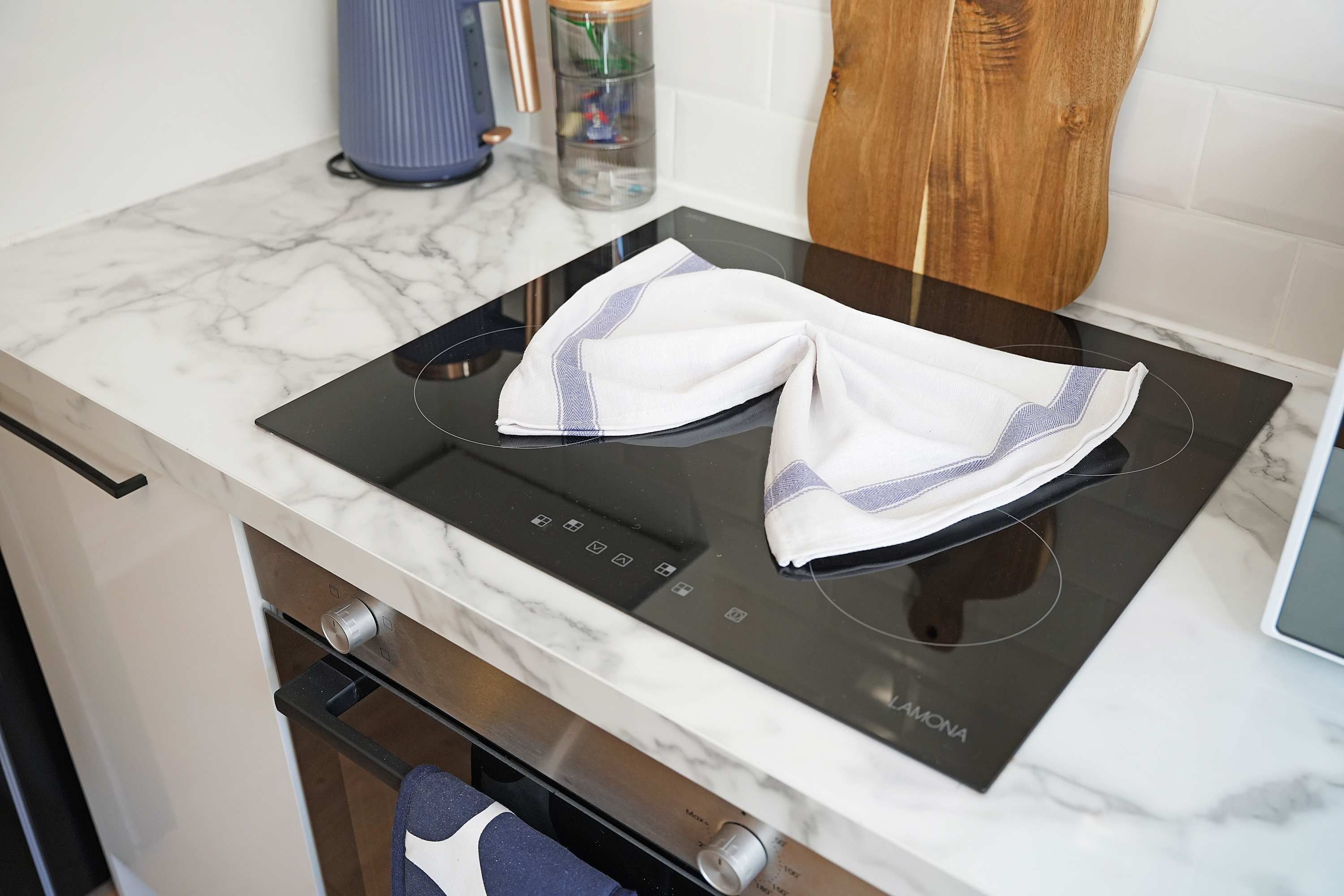 Una cocina con tope de inducción negro, encimera de mármol blanco y mueble de madera.