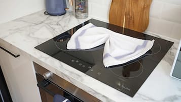 Una cocina con tope de inducción negro, encimera de mármol blanco y mueble de madera.