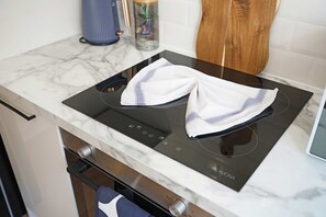 A kitchen with a black induction cooktop, a white marble countertop, and a wooden cabinet. - Stylish 4BR Doncaster Sleeps 8 by Stay With Us (Doncaster)