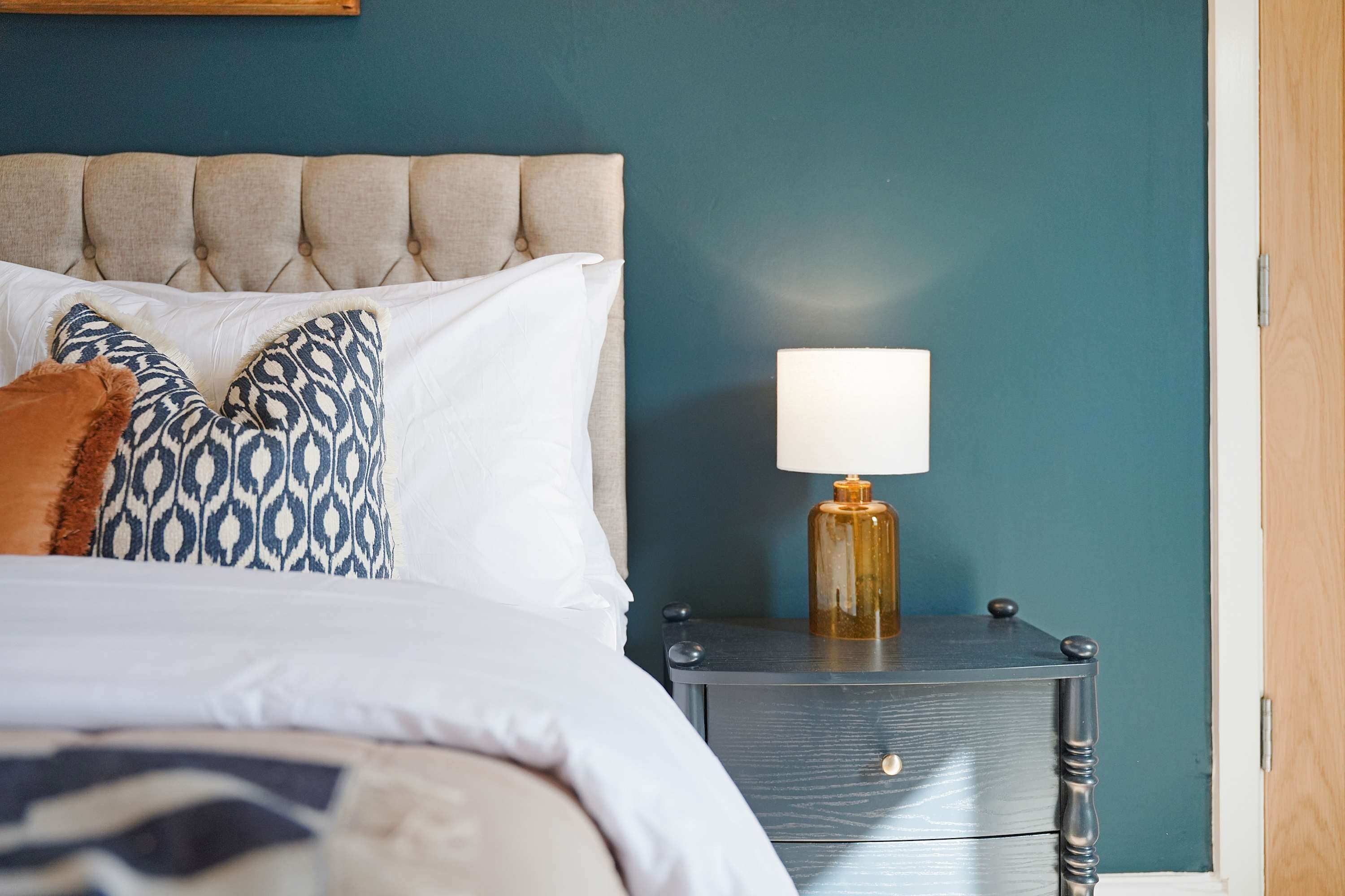 A neatly made bed with patterned pillows, a bedside lamp, and a dark wooden nightstand.