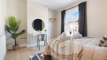 A bedroom with a bed, a desk, a chair, a mirror, and a window with curtains.