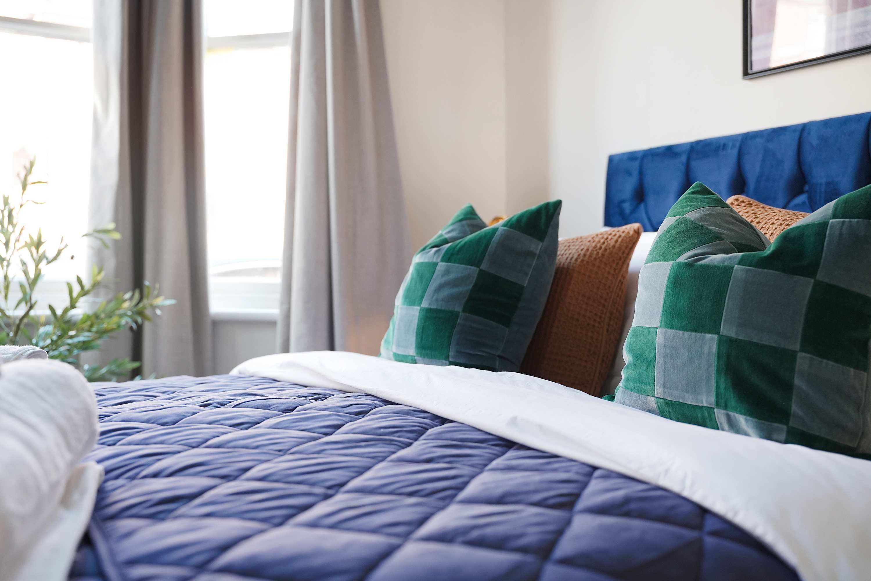 Un lit bien fait, avec une couette bleue, un oreiller blanc et deux oreillers verts et bruns.