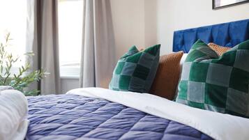 Un lit bien fait, avec une couette bleue, un oreiller blanc et deux oreillers verts et bruns.