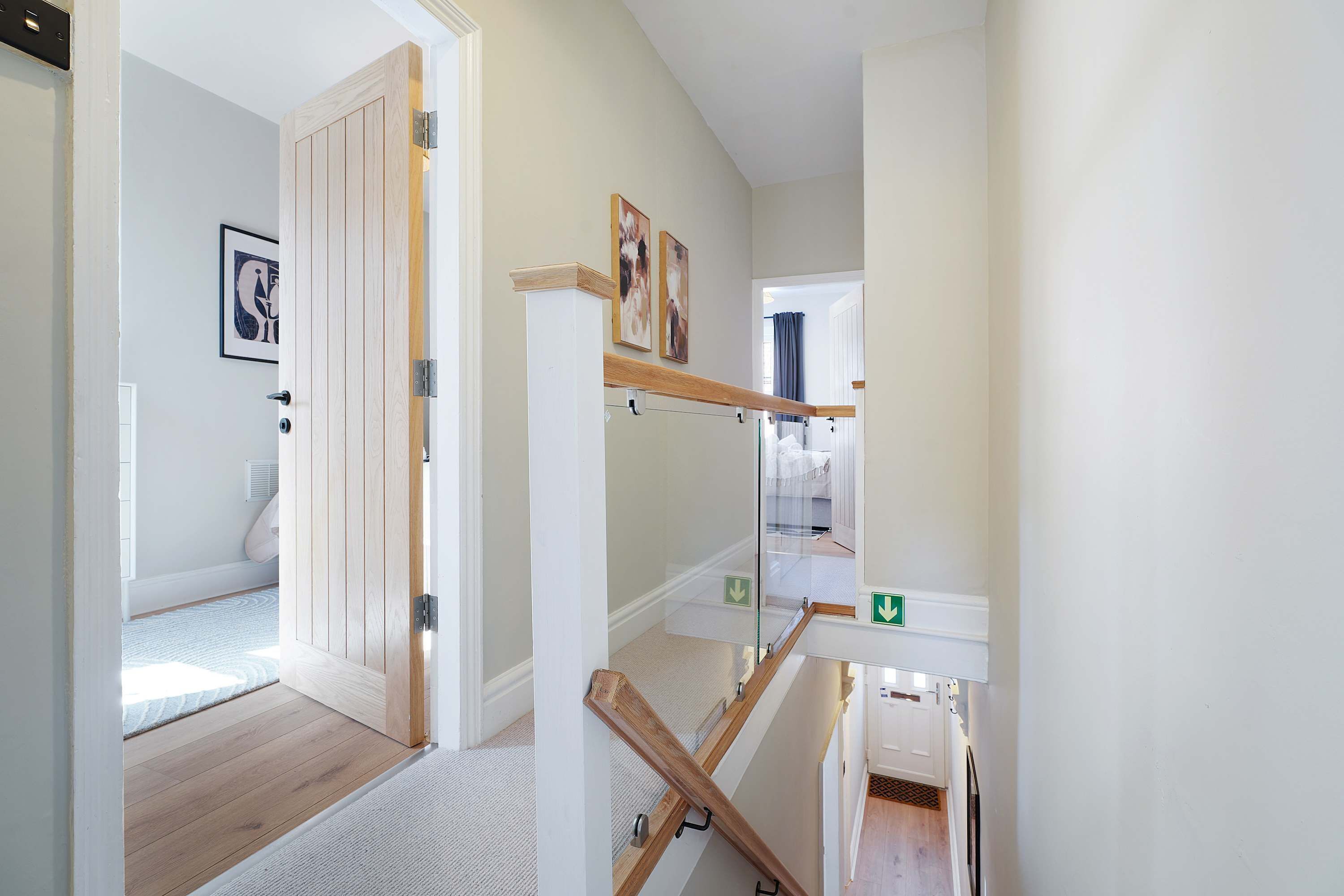 Un pasillo con piso de madera, una puerta con manija metálica y una escalera con barandilla de madera.