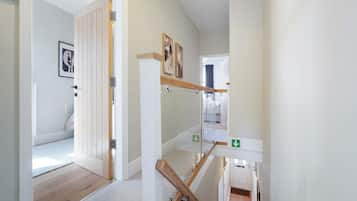 Un pasillo con piso de madera, una puerta con manija metálica y una escalera con barandilla de madera.