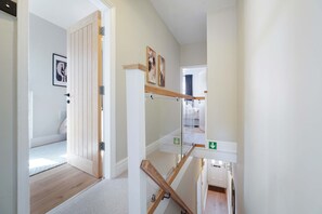 A hallway with a wooden floor, a door with a metal handle, and a staircase with a wooden handrail. - Stylish 4BR Doncaster Sleeps 8 by Stay With Us (Doncaster)