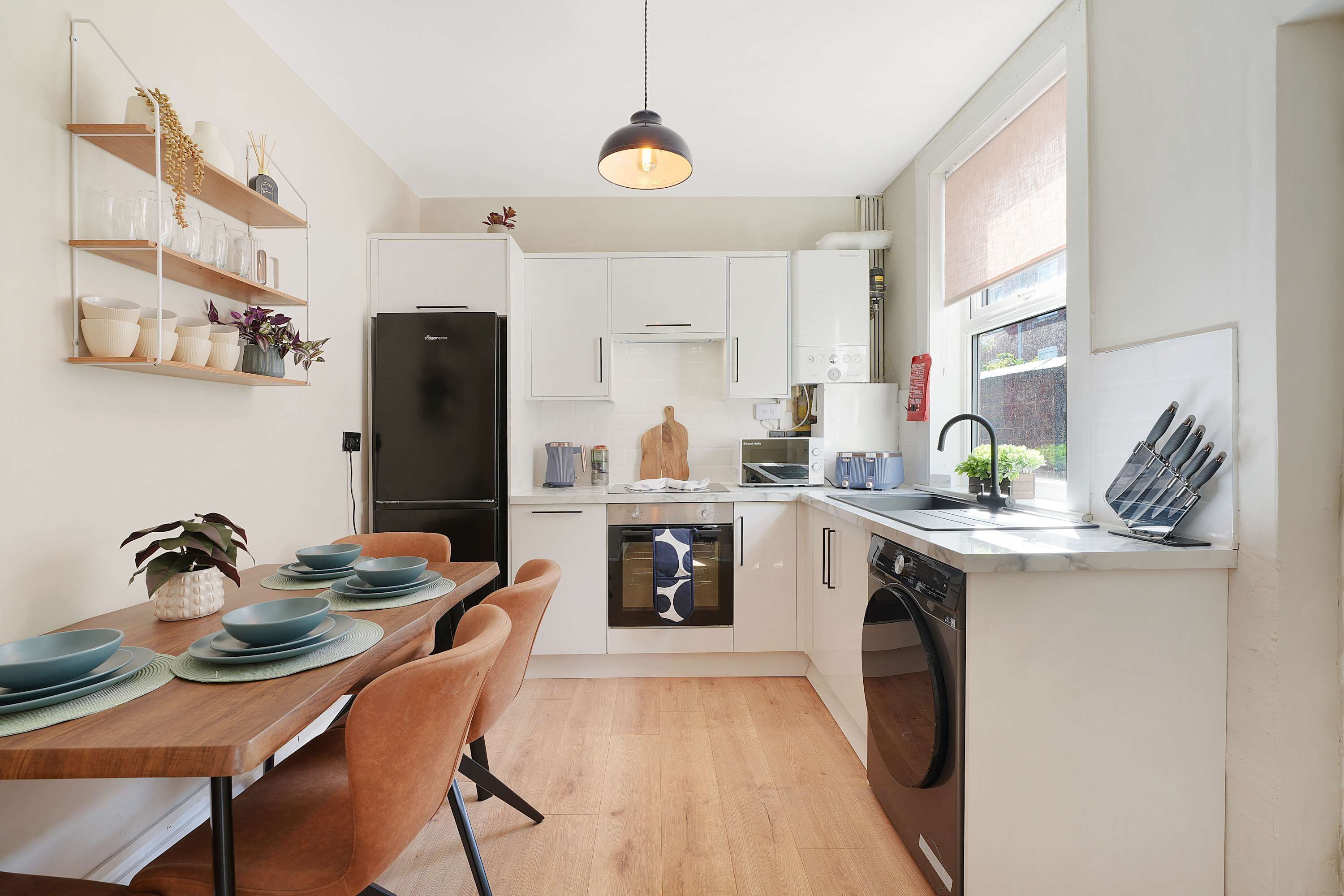 Una cocina moderna con armarios blancos, un refrigerador negro, una mesa de comedor con platos azules y una lámpara colgante.