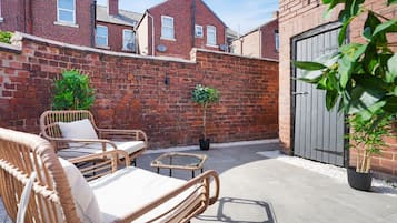 Un muro de ladrillo con una reja, un patio con mobiliario de mimbre y una planta en maceta.