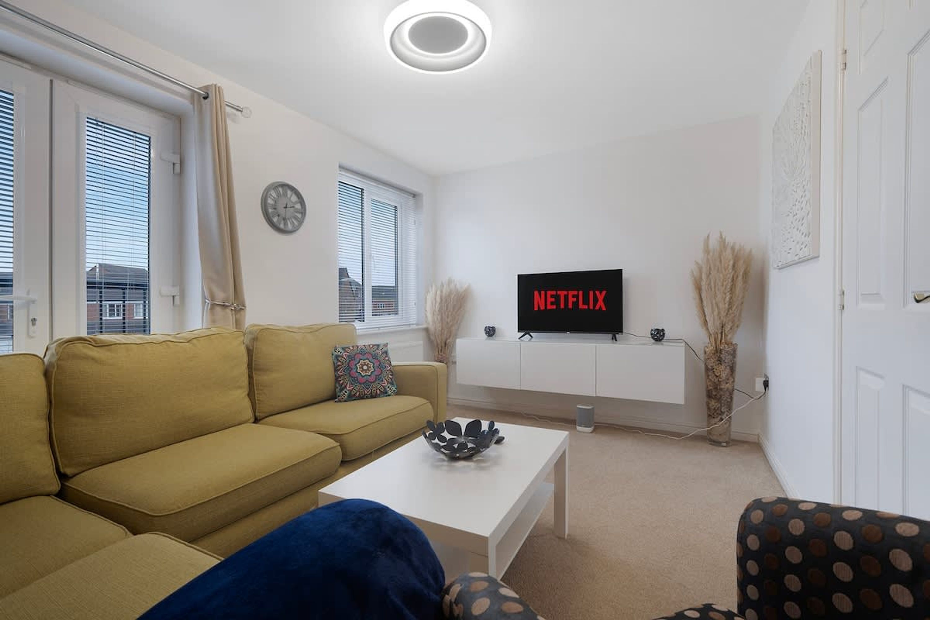 Ein Wohnzimmer mit einer Couch, einem Couchtisch und einem Fernseher, der 'NETFLIX' anzeigt.