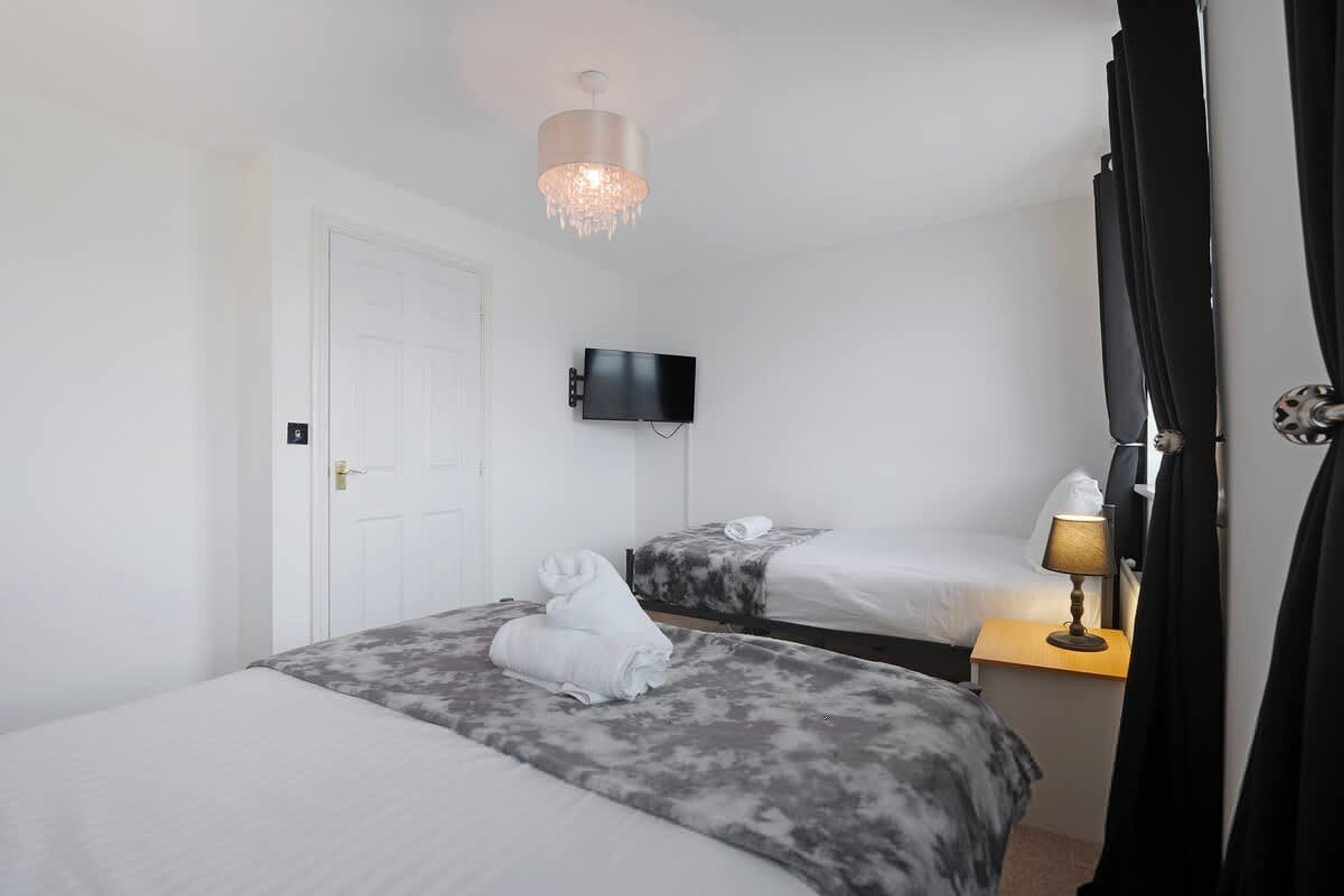 A hotel room with two beds, a flat-screen TV, a bedside lamp, and a chandelier.