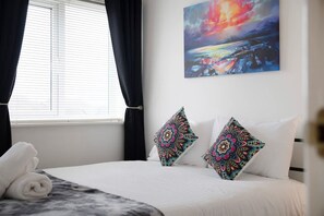 Ein Hotelzimmer mit einem Bett, zwei Zierkissen, einem Bild an der Wand und einem Vorhangfenster.