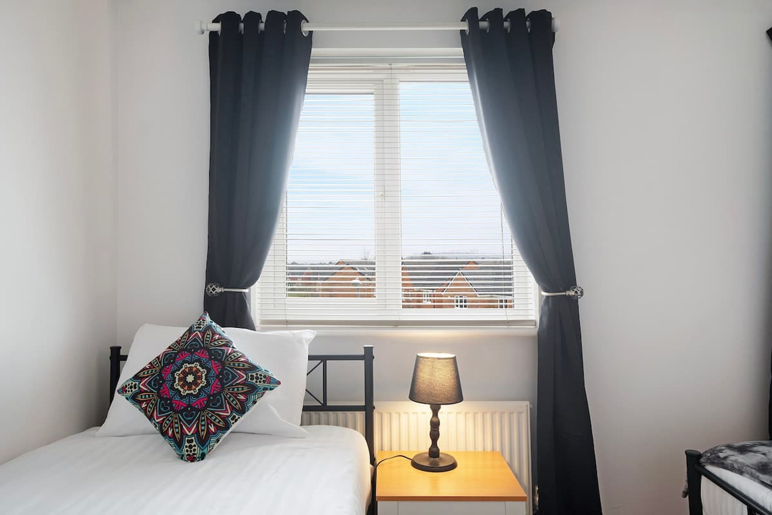 A bedroom with a bed, a bedside table with a lamp, and a window with curtains.