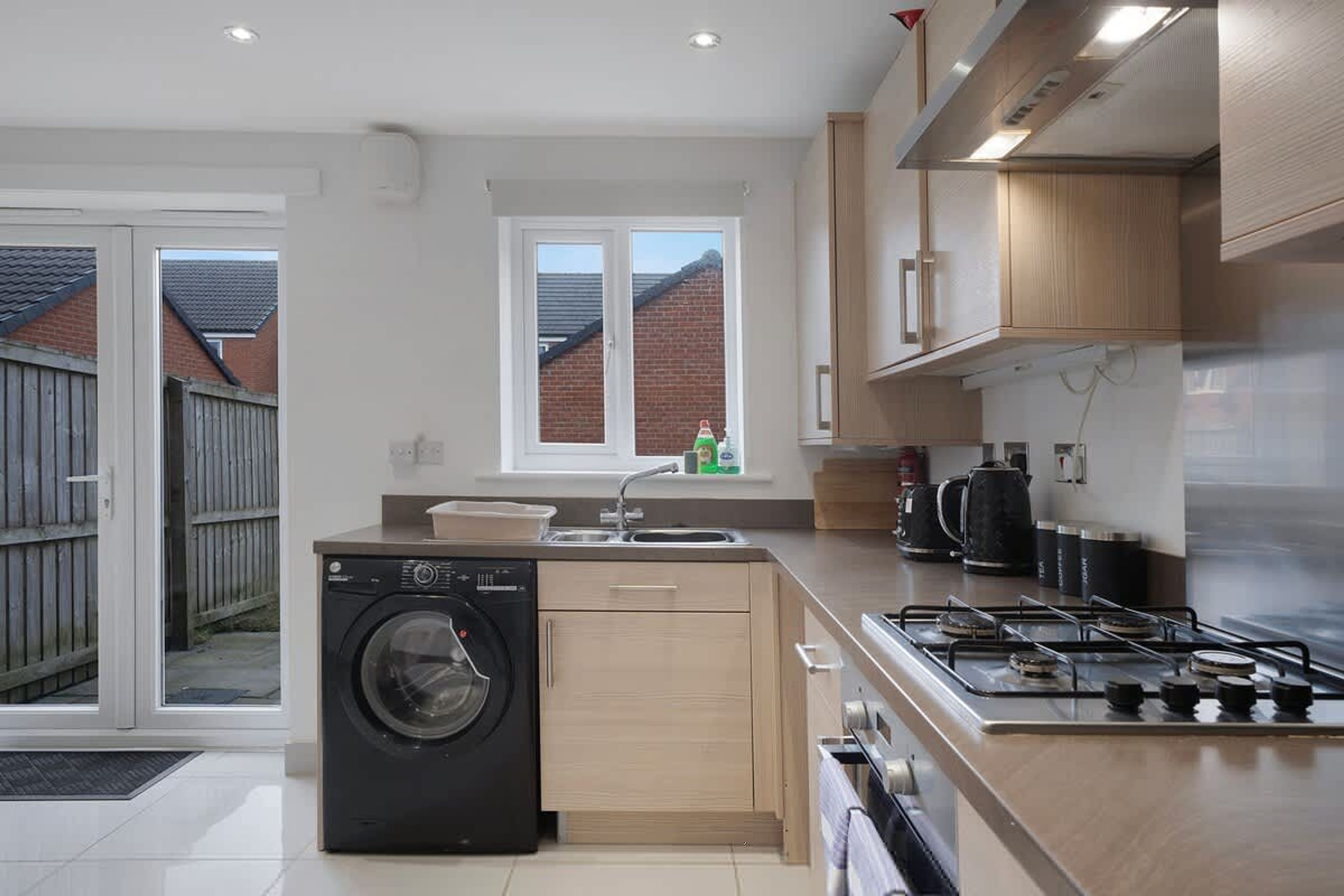 Une cuisine moderne équipée d’un lave-linge intégré, d’une cuisinière à gaz et d’une fenêtre donnant sur un quartier résidentiel.