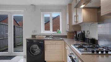 Une cuisine moderne équipée d’un lave-linge intégré, d’une cuisinière à gaz et d’une fenêtre donnant sur un quartier résidentiel.