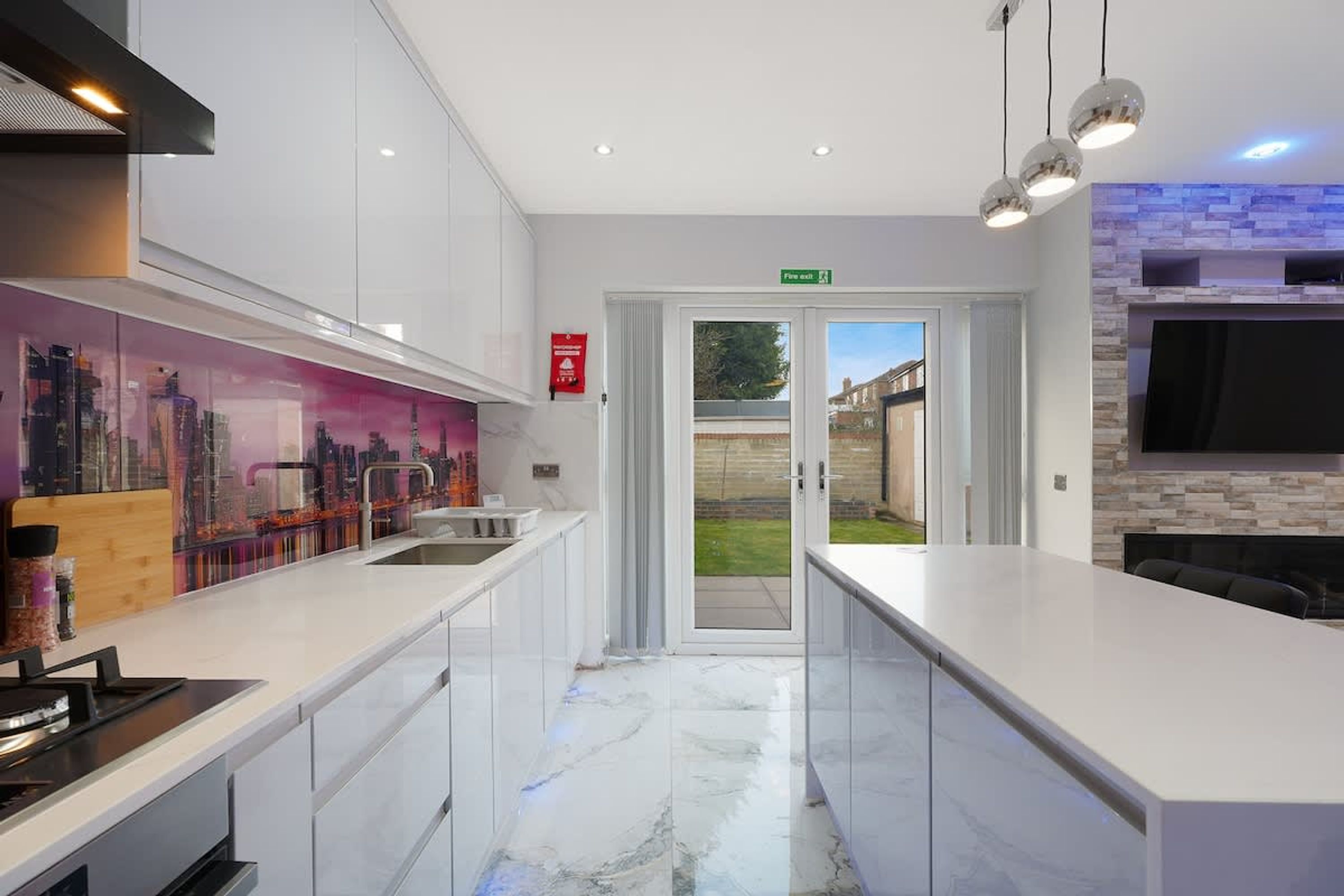 A modern kitchen with white cabinetry, a marble countertop, and a cityscape mural.