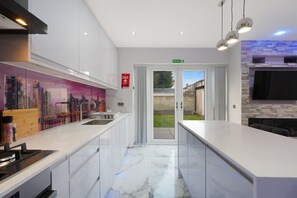 A modern kitchen with white cabinetry, a marble countertop, and a cityscape mural. - Stylish Home With Parking and Easy City Access (Manchester)