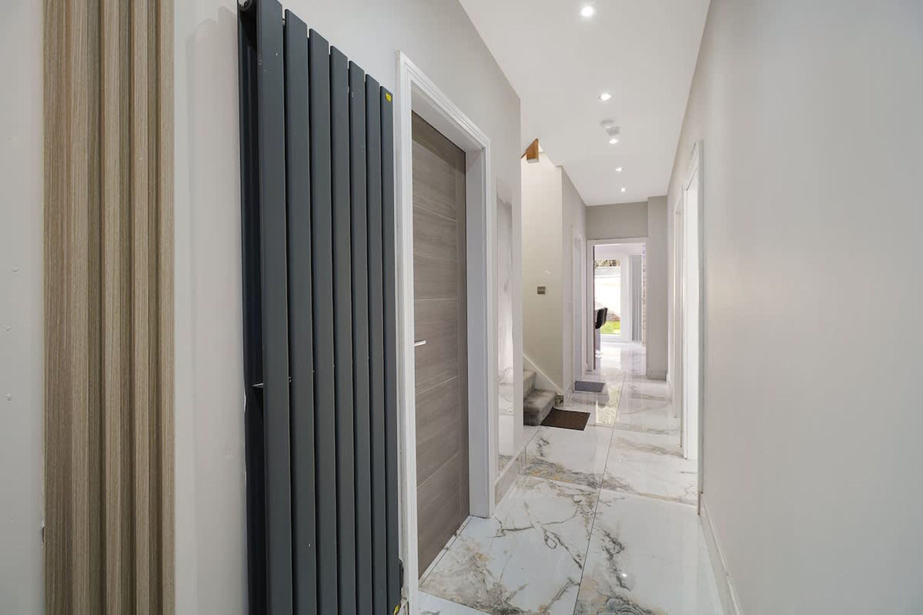 Un pasillo con una puerta, una escalera y vista a otra habitación.