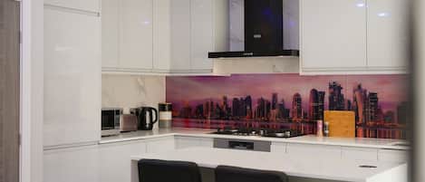 A modern kitchen with white cabinetry, a black range hood, and a cityscape mural on the backsplash.