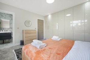 A modern bedroom with a bed, a wardrobe, a mirror, and a bathroom. - Stylish Home With Parking and Easy City Access (Manchester)