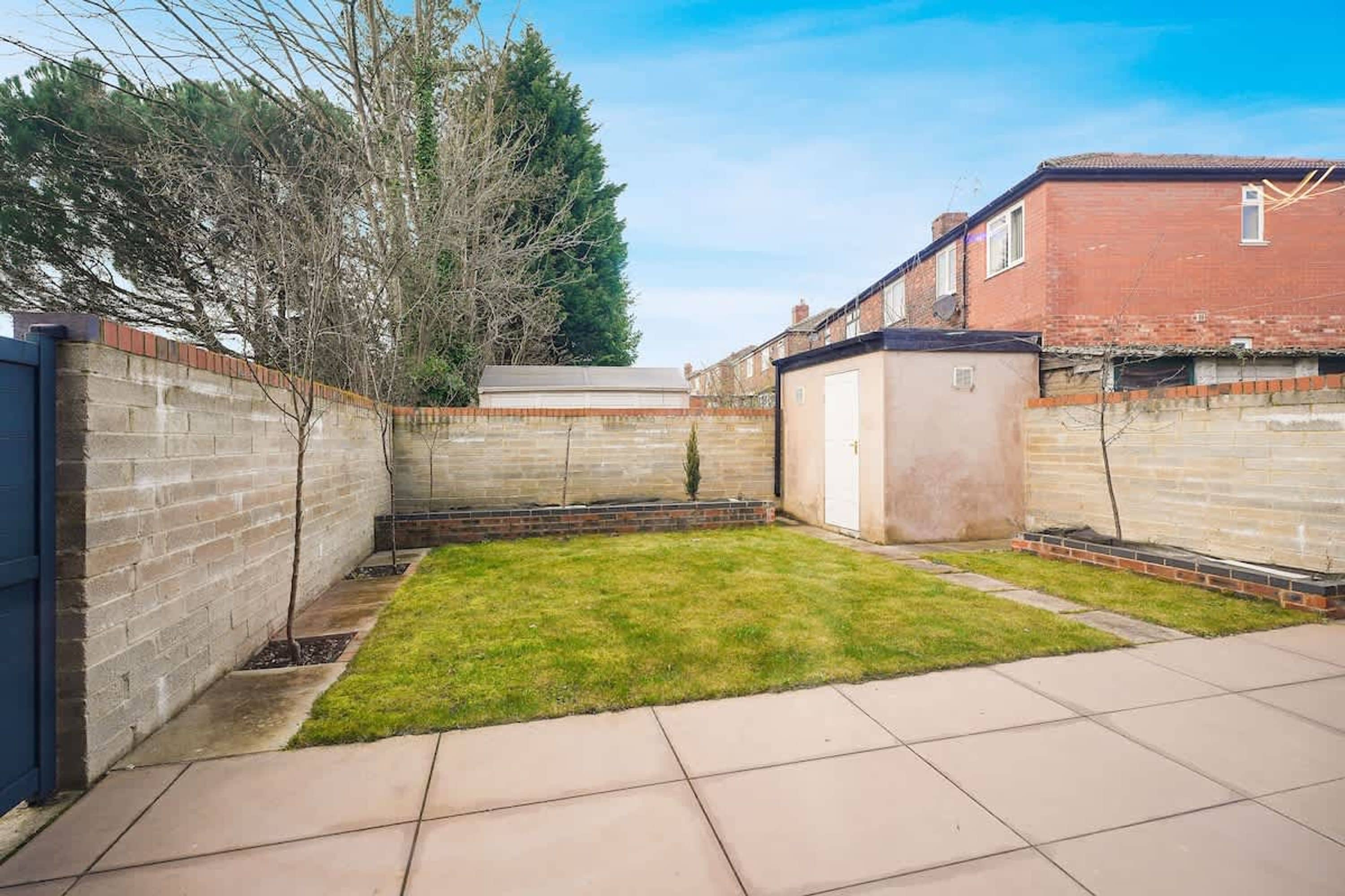 A residential backyard with a paved patio, a grassy lawn, and a brick wall.